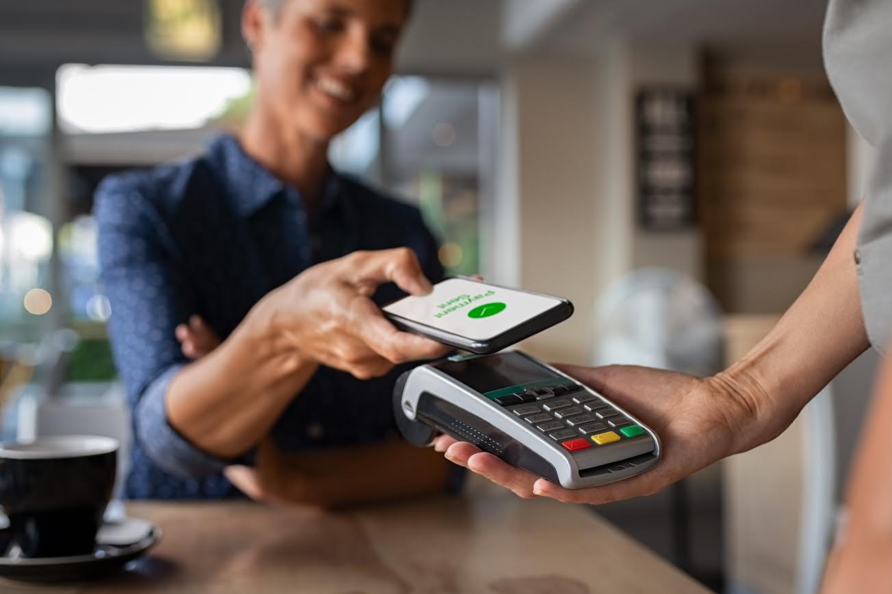 Woman paying bill through smartphone using NFC technology in a restaurant. Satisfied customer paying through mobile phone using contactless technology. Closeup hands of mobile payment at a coffee shop